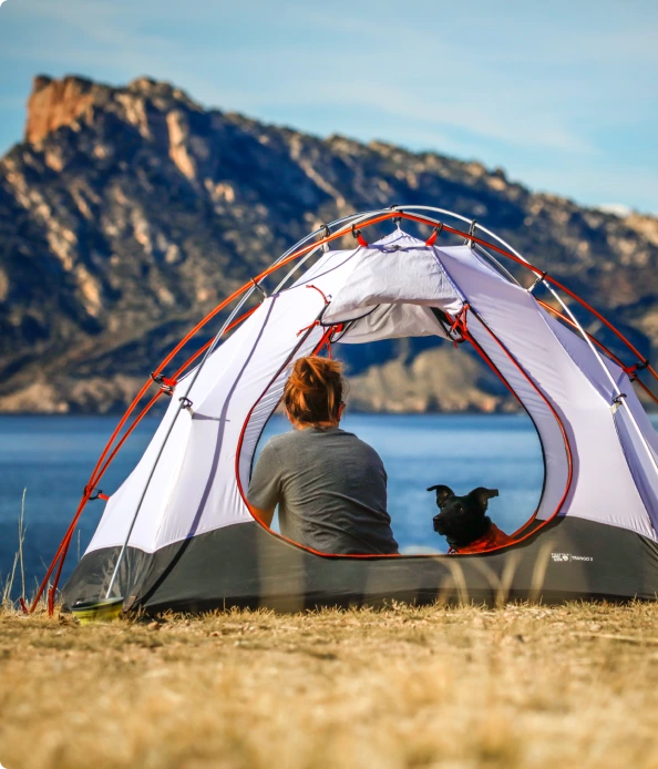 A woman and a dog sitting in a tent, in nature